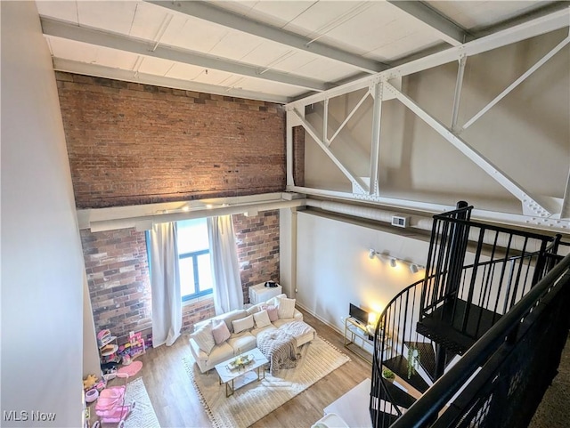 interior space with beamed ceiling, brick wall, wood-type flooring, and high vaulted ceiling