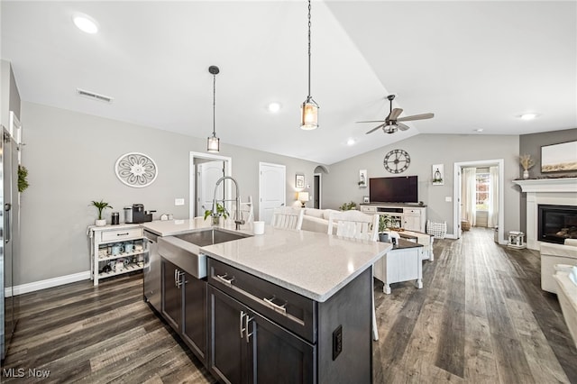 kitchen featuring decorative light fixtures, sink, light stone counters, dark wood-type flooring, and a center island with sink