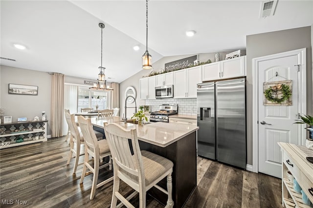 kitchen featuring a breakfast bar, white cabinetry, vaulted ceiling, appliances with stainless steel finishes, and a kitchen island with sink