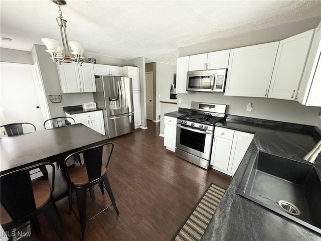 kitchen featuring appliances with stainless steel finishes, pendant lighting, white cabinetry, sink, and dark hardwood / wood-style flooring