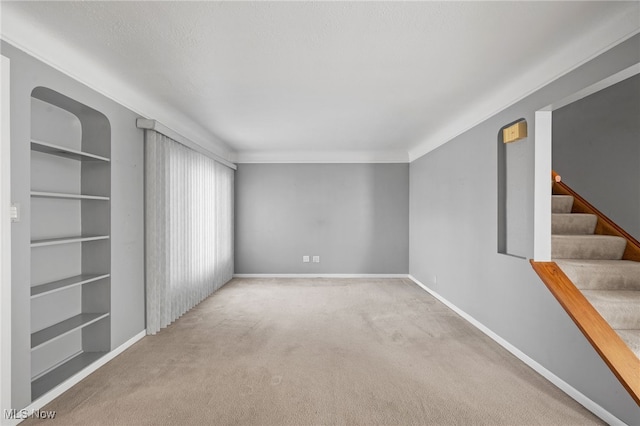 spare room featuring light carpet, a textured ceiling, and built in shelves