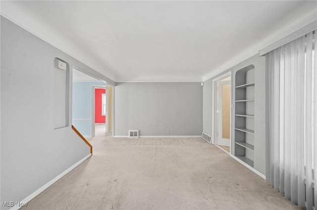 unfurnished room featuring light colored carpet and built in features