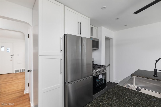 kitchen featuring sink, appliances with stainless steel finishes, white cabinetry, dark stone countertops, and wood-type flooring