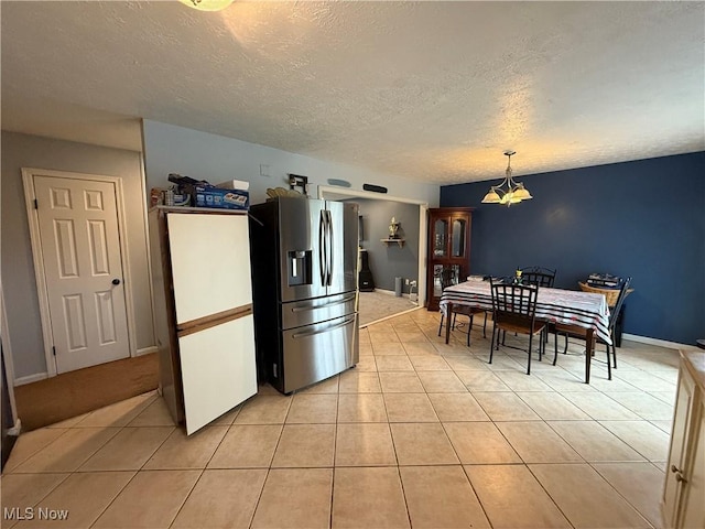 kitchen featuring a textured ceiling, hanging light fixtures, light tile patterned floors, stainless steel fridge, and a notable chandelier