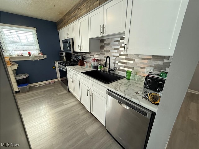 kitchen with stainless steel appliances, white cabinetry, light stone countertops, and sink