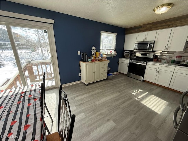 kitchen featuring a textured ceiling, light wood-type flooring, white cabinets, and appliances with stainless steel finishes