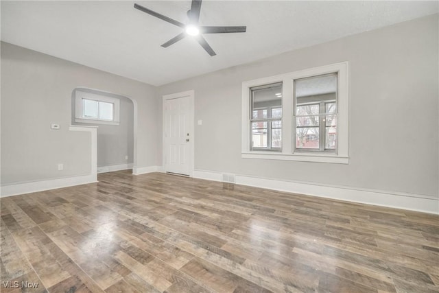 spare room with baseboards, visible vents, arched walkways, ceiling fan, and wood finished floors