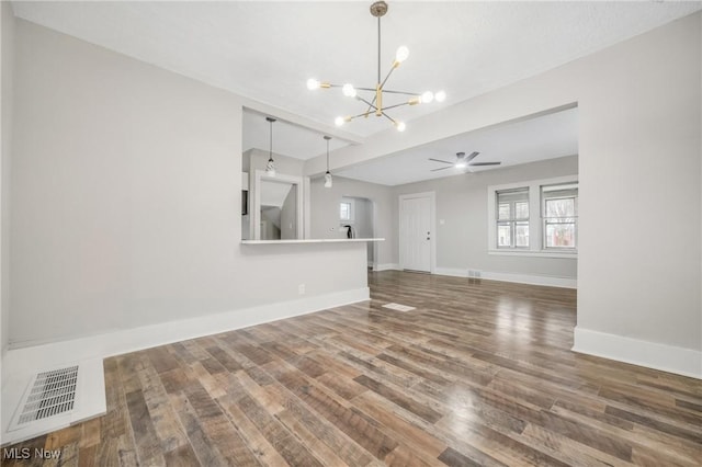 unfurnished room with ceiling fan with notable chandelier, visible vents, baseboards, and wood finished floors