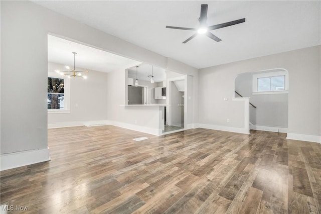 unfurnished living room with baseboards, arched walkways, wood finished floors, stairs, and ceiling fan with notable chandelier