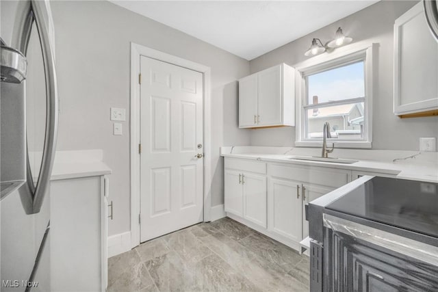 kitchen with light countertops, a sink, freestanding refrigerator, and white cabinets