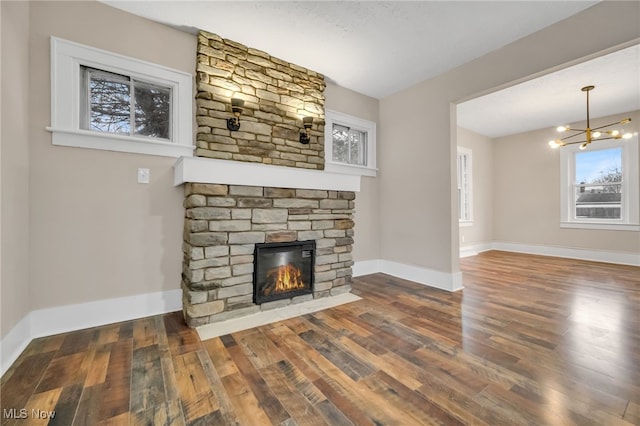 unfurnished living room with a stone fireplace, an inviting chandelier, wood finished floors, and baseboards