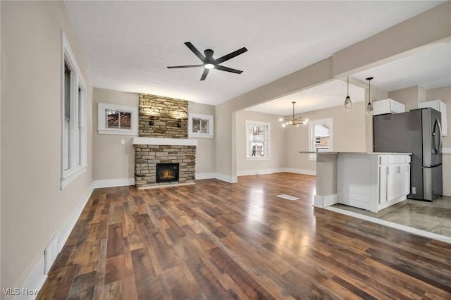 unfurnished living room featuring ceiling fan with notable chandelier, a fireplace, wood finished floors, and baseboards