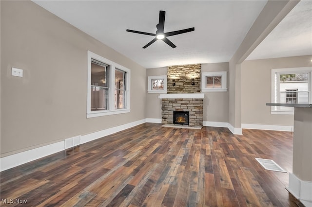 unfurnished living room featuring hardwood / wood-style floors, a stone fireplace, visible vents, and baseboards