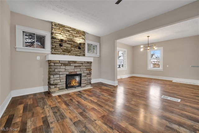 unfurnished living room with baseboards, visible vents, wood finished floors, a fireplace, and a chandelier