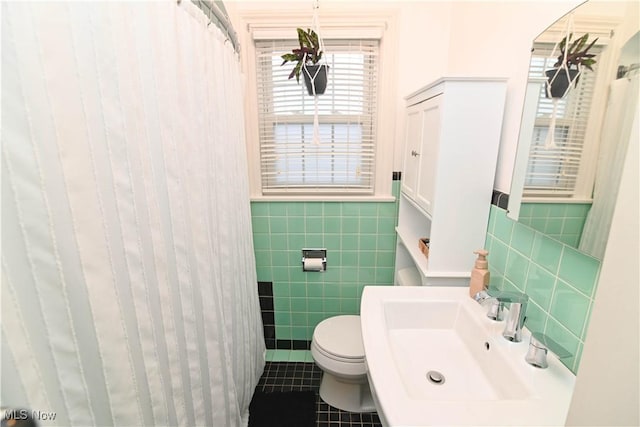 bathroom with toilet, tile patterned flooring, sink, and tile walls