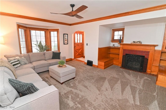 living room with a tiled fireplace, ornamental molding, carpet floors, and ceiling fan