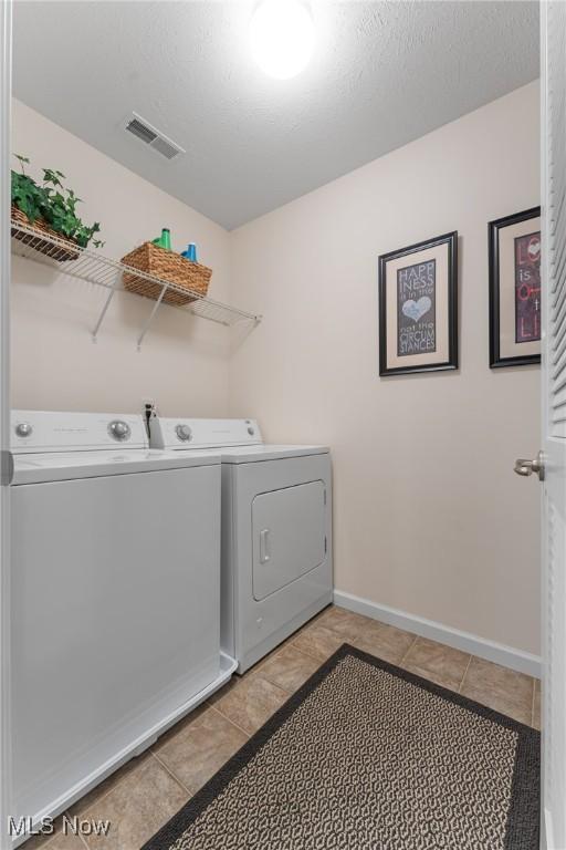 clothes washing area featuring separate washer and dryer, a textured ceiling, and light tile patterned flooring