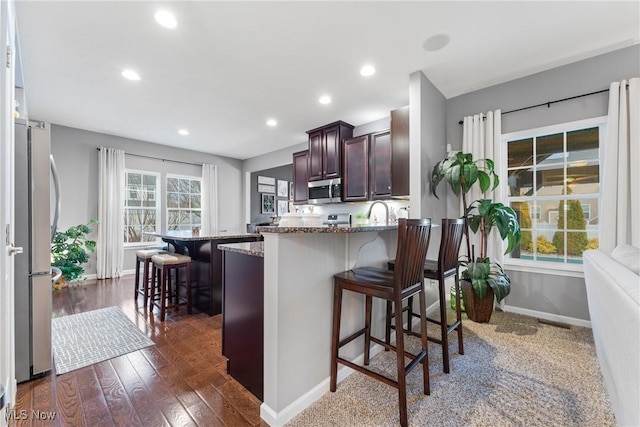 kitchen with a breakfast bar, appliances with stainless steel finishes, dark hardwood / wood-style floors, a kitchen island, and light stone countertops