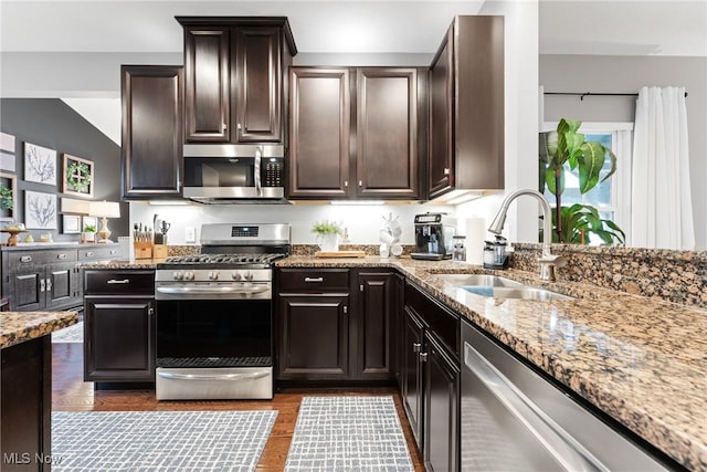 kitchen featuring dark brown cabinetry, sink, light stone counters, appliances with stainless steel finishes, and light hardwood / wood-style floors