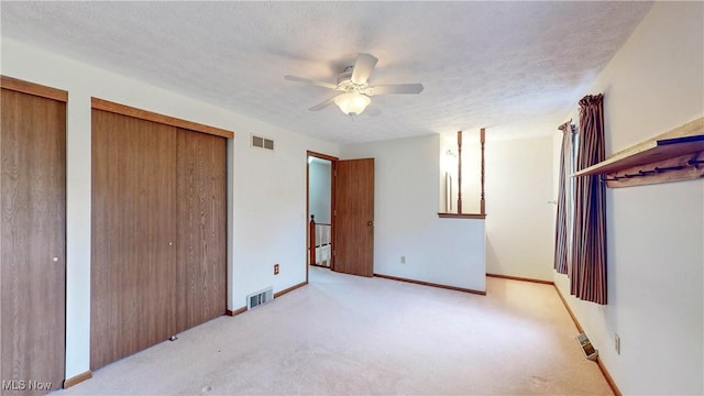 unfurnished bedroom with multiple closets, light colored carpet, a textured ceiling, and ceiling fan