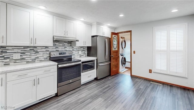 kitchen featuring stainless steel appliances, stacked washer / dryer, white cabinets, decorative backsplash, and light wood-type flooring