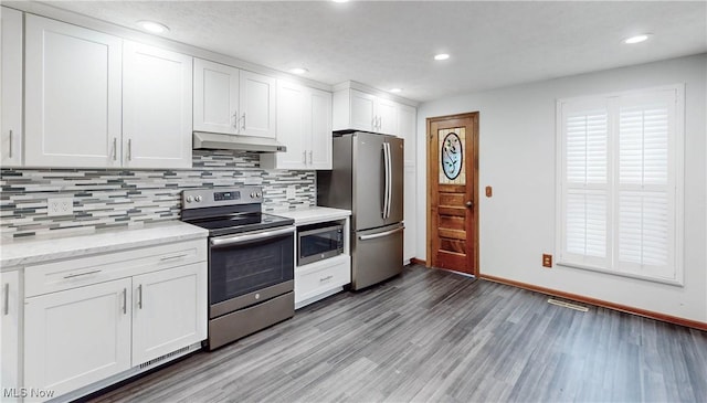 kitchen with dark wood-type flooring, appliances with stainless steel finishes, backsplash, light stone countertops, and white cabinets