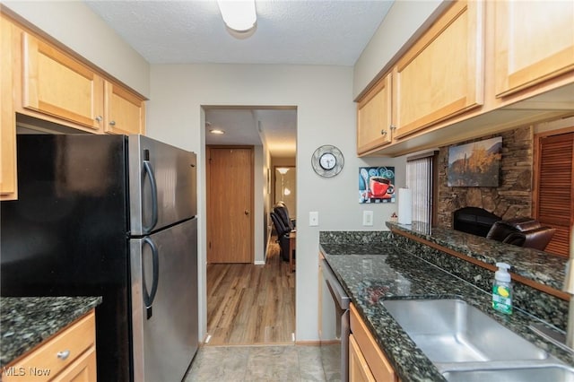 kitchen featuring sink, stainless steel appliances, a textured ceiling, a stone fireplace, and dark stone counters