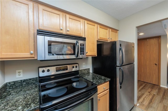 kitchen with light hardwood / wood-style flooring, appliances with stainless steel finishes, dark stone countertops, a textured ceiling, and light brown cabinetry