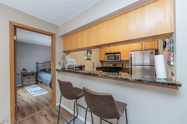 kitchen featuring a breakfast bar area, dark stone countertops, kitchen peninsula, stainless steel appliances, and light wood-type flooring