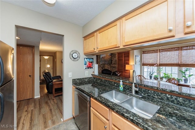 kitchen featuring sink, appliances with stainless steel finishes, a textured ceiling, a stone fireplace, and dark stone counters