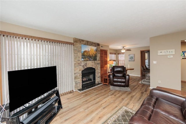 living room with a stone fireplace, light hardwood / wood-style flooring, and ceiling fan