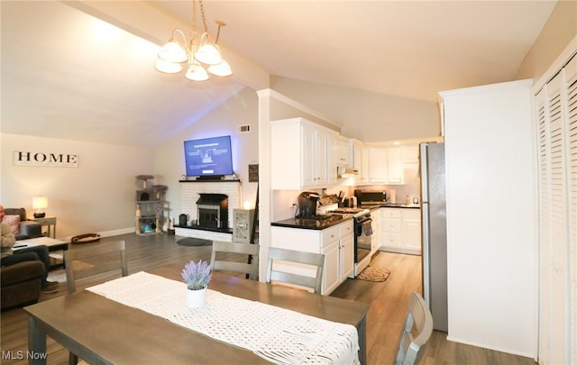 dining space with lofted ceiling, a chandelier, hardwood / wood-style floors, and a fireplace