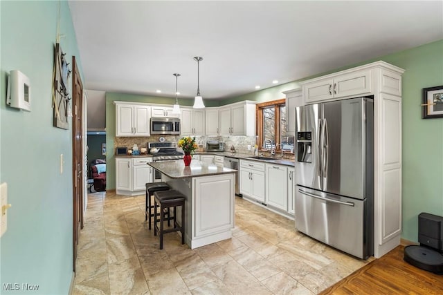 kitchen featuring appliances with stainless steel finishes, a breakfast bar, decorative light fixtures, sink, and a center island