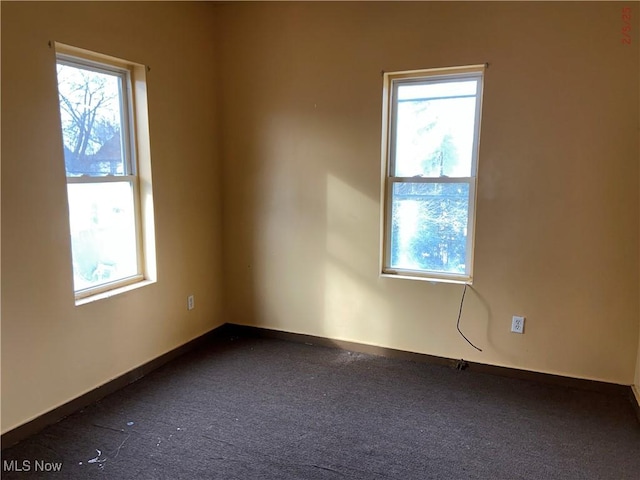 spare room with a healthy amount of sunlight and dark colored carpet