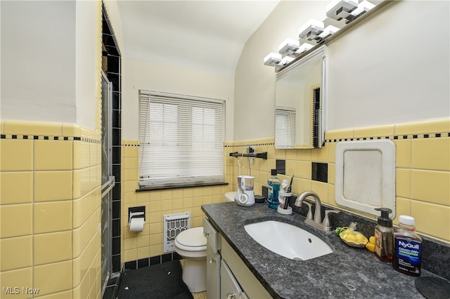 bathroom with vanity, toilet, heating unit, and tile walls