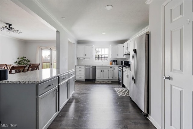 kitchen with sink, white cabinetry, stainless steel appliances, ornamental molding, and dark hardwood / wood-style flooring