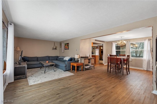 living area with a textured ceiling, baseboards, wood finished floors, and an inviting chandelier