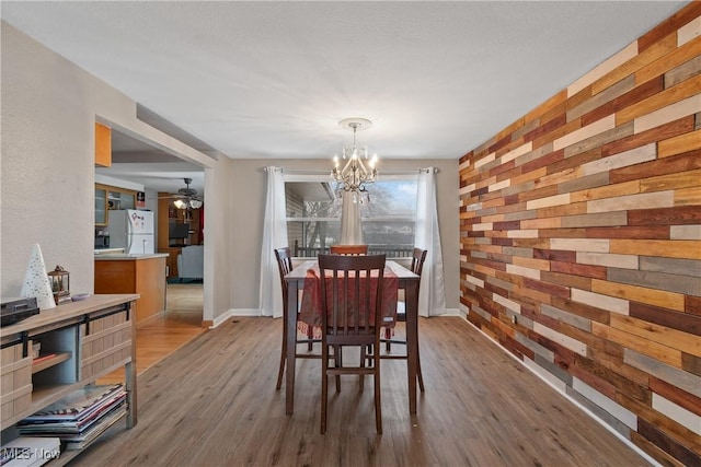 dining area featuring a chandelier, wood walls, wood finished floors, and baseboards