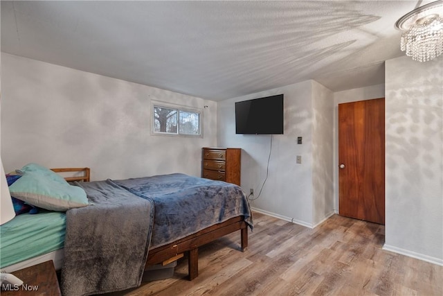 bedroom featuring light wood-type flooring, a notable chandelier, and baseboards