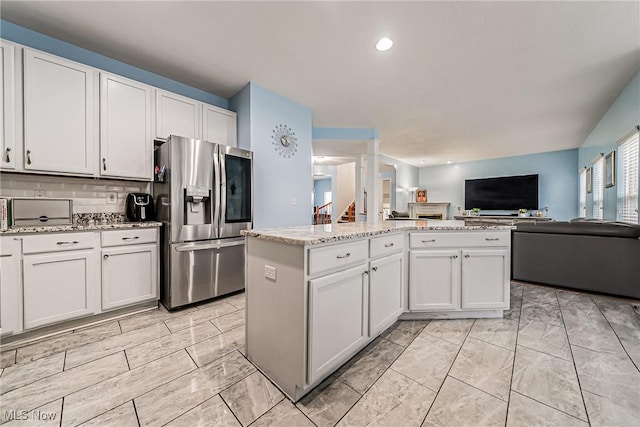 kitchen featuring a kitchen island, tasteful backsplash, white cabinets, stainless steel fridge, and light stone counters