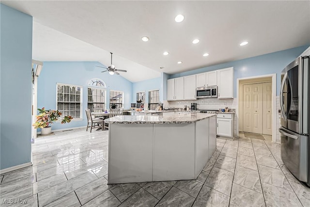 kitchen featuring lofted ceiling, a kitchen island, stainless steel appliances, light stone countertops, and white cabinets