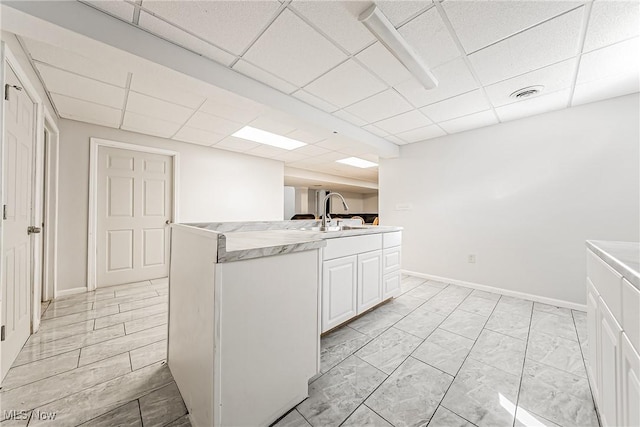 kitchen featuring a drop ceiling, sink, and white cabinets