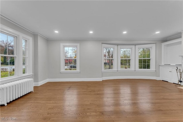 unfurnished living room featuring radiator heating unit, ornamental molding, and light hardwood / wood-style floors