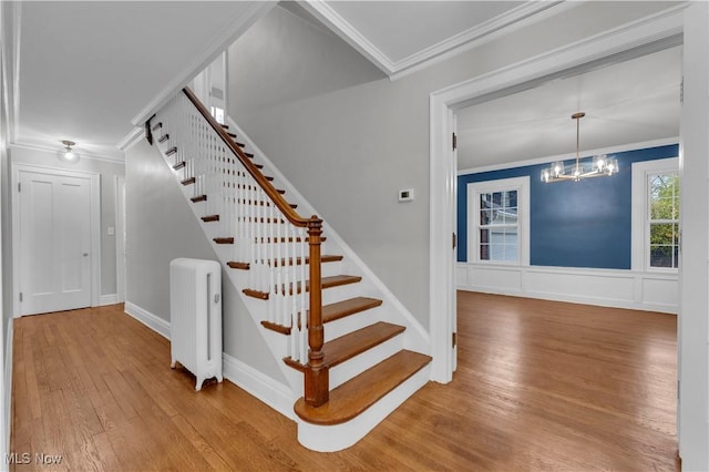 stairway with hardwood / wood-style floors, crown molding, radiator heating unit, and an inviting chandelier