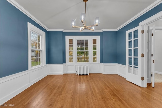 unfurnished dining area with an inviting chandelier, crown molding, radiator, and light hardwood / wood-style floors