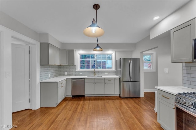 kitchen featuring pendant lighting, sink, gray cabinets, light hardwood / wood-style flooring, and stainless steel appliances