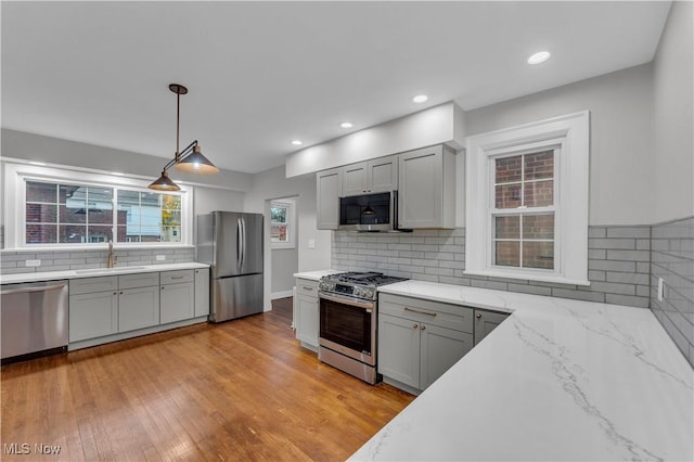 kitchen with sink, gray cabinets, appliances with stainless steel finishes, light hardwood / wood-style floors, and decorative light fixtures