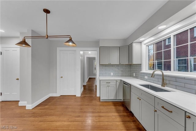 kitchen with pendant lighting, sink, gray cabinets, light hardwood / wood-style flooring, and dishwasher