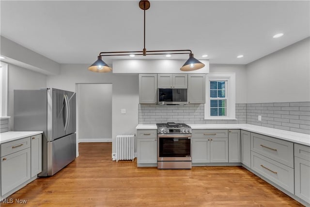 kitchen featuring radiator, gray cabinets, appliances with stainless steel finishes, hanging light fixtures, and light hardwood / wood-style floors