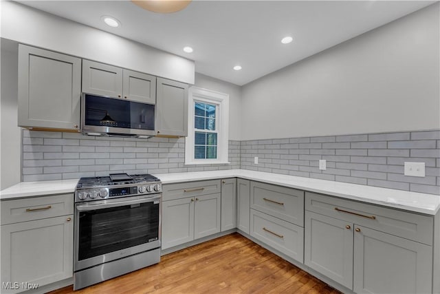 kitchen featuring appliances with stainless steel finishes, gray cabinetry, backsplash, and light hardwood / wood-style flooring